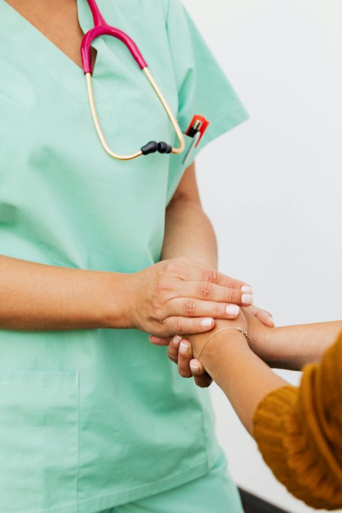 A nurse in green scrubs gently clasps a patient's hand, offering support.